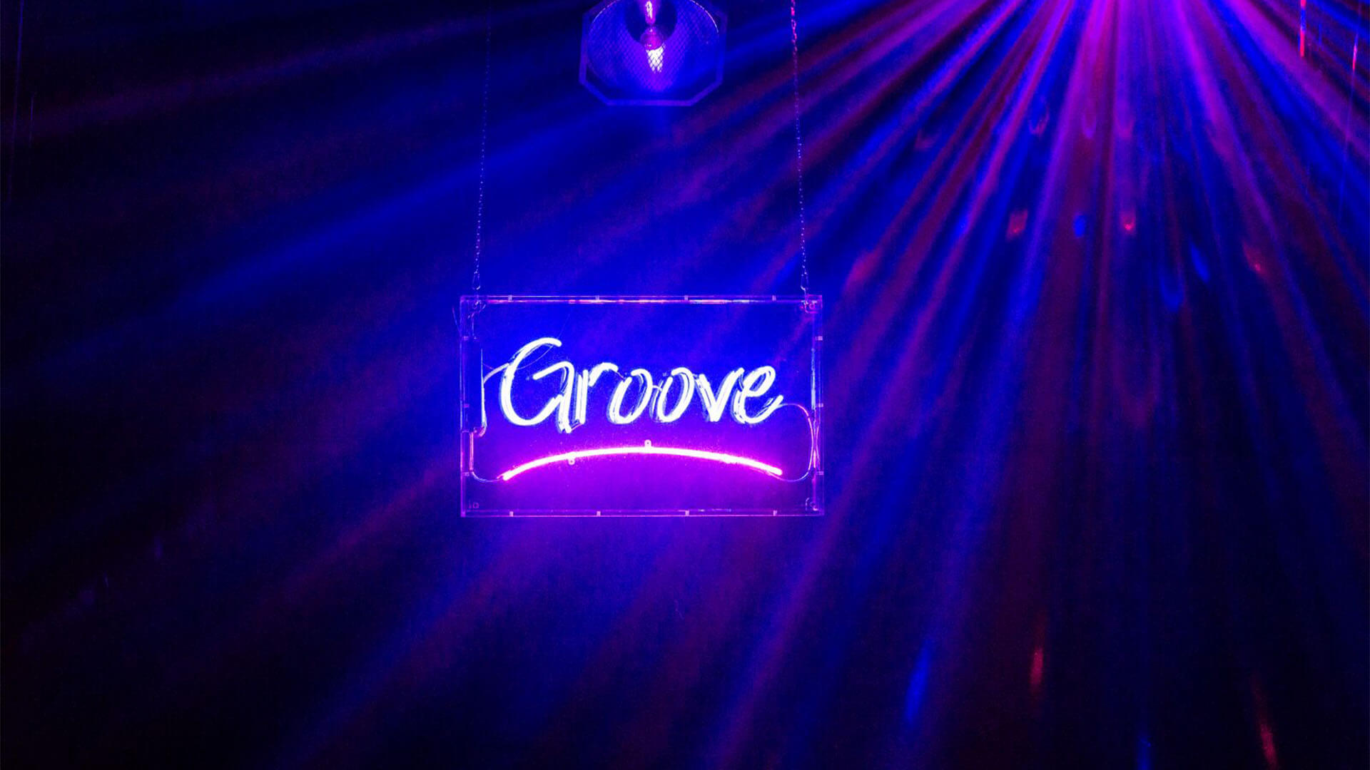 A neon sign hangs from the ceiling that reads: “Groove”. The word glows in blue and there is a red line underneath it.